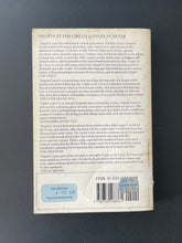 Load image into Gallery viewer, Nights at the Circus by Angela Carter: photo of the back cover which shows scuff marks, minor discolouring, and a small patch missing off the cover, towards the bottom, along the spine. This missing patch also wraps around to the spine.