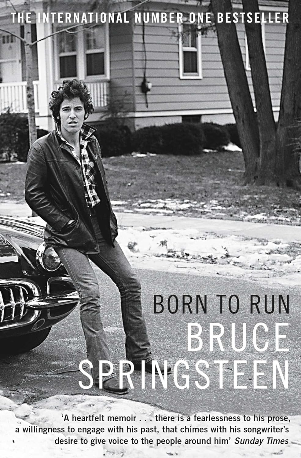 Born to Run by Bruce Springsteen: stock image of front cover which shows a young Bruce Springsteen leaning against a car in front of a suburban home.

