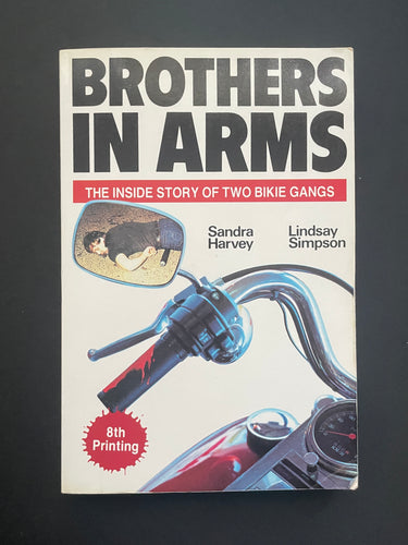 Book cover of 'Brothers in Arms' by Sandra Harvey & Lindsay Simpson with motorcycle image on a dark background. There are some minor scuff marks along the edges, and some creasing on the bottom-right corner. 