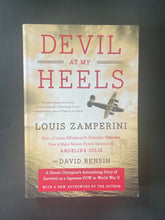 Load image into Gallery viewer, Devil at My Heels by Louis Zamperini: photo of the front cover which shows very fine creases running down the left-hand side, and very fine creasing on the top-right corner, none of which is overly noticeable.
