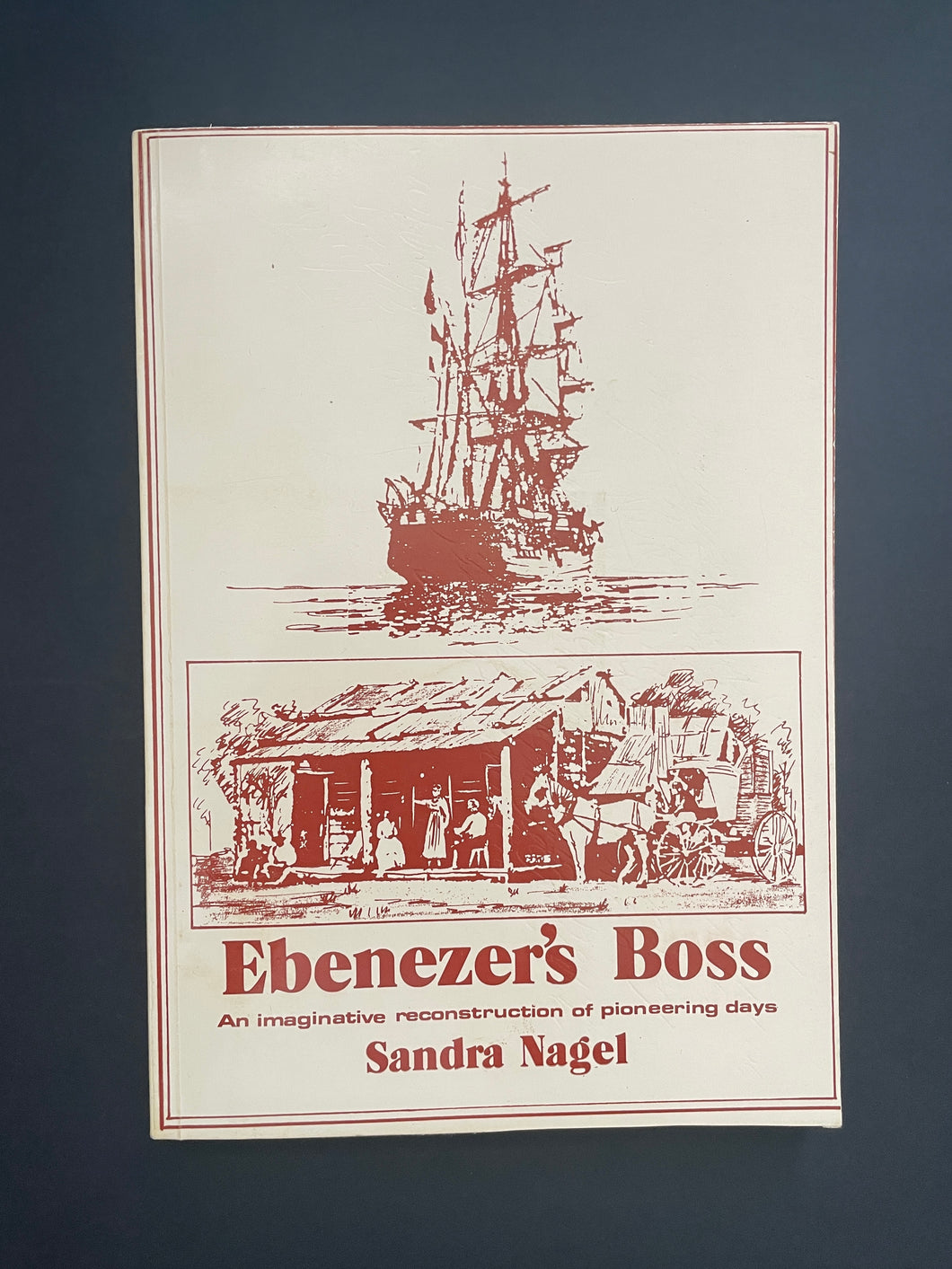 Book cover of 'Ebenezer's Boss' by Sandra Nagel with ship and pioneer village illustration on a dark background. The photo shows very minor scuff marks along the edges.