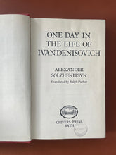 Load image into Gallery viewer, One Day in the Life of Ivan Denisovich: photo of the title page which has a black library stamp on the bottom of the page.
