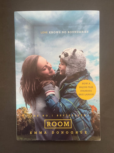 Book cover of 'Room' by Emma Donoghue featuring a woman and child against a cloudy sky. Photo shows tiny scuff marks along the edges.