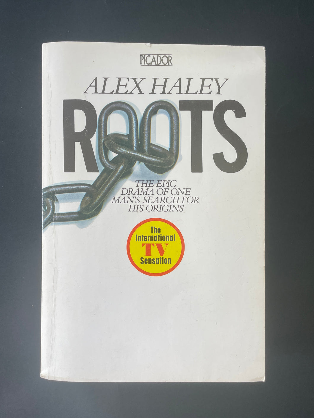 Roots by Alex Haley: photo of the front cover which shows very minor scuff marks along the edges, and minor creasing running down the left-hand side of the book, parallel to the spine.