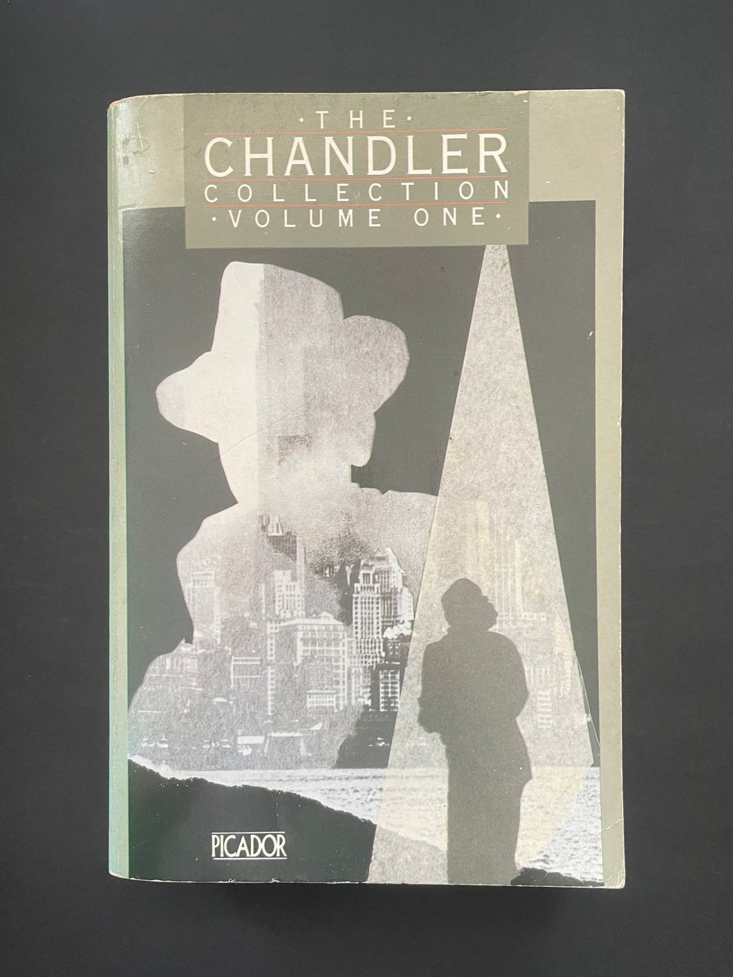 Book cover of 'The Chandler Collection Volume One' by Raymond Chandler with a silhouette design on a dark background. The photo shows minor scuff marks and scratching, and a minor crease on the bottom-right corner.