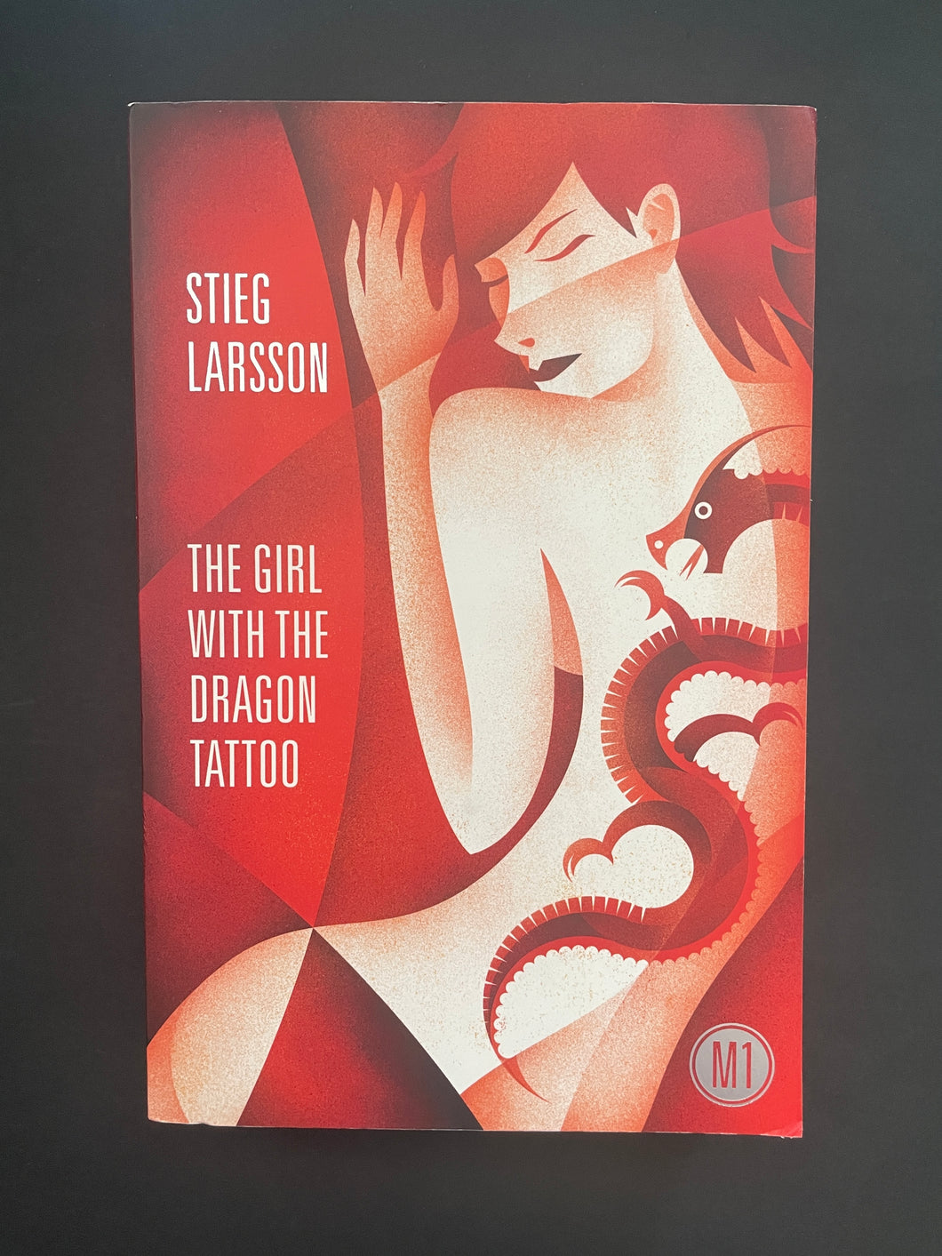 Book cover of 'The Girl with the Dragon Tattoo' by Stieg Larsson featuring a stylized illustration of a woman and a dragon. Photo shows minor scuff marks along the edges.