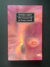 Load image into Gallery viewer, The book cover of 'The Unusual Life of Tristan Smith' by Peter Carey, featuring a textured, abstract pink and orange cover with a black title box, photographed on a dark background. The photo shows very minor scuff marks along the edges.
