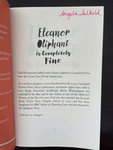 Load image into Gallery viewer, Eleanor Oliphant is Completely Fine by Gail Honeyman book: photo of the first page, at the top of which a previous owner has written their name in pink pen.
