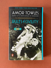 Load image into Gallery viewer, Rules of Civility by Amor Towles: photo of the front cover which shows very minor (barely visible) scuff marks along the edges of the inner (blue) cover.
