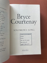 Load image into Gallery viewer, Solomon&#39;s Song by Bryce Courtenay: photo of the title page which has a black, square shaped stamp on the bottom-half of the page. 
