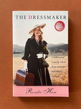 Load image into Gallery viewer, The Dressmaker by Rosalie Ham: photo of the front cover which shows very minor (barely visible) scuff marks along the edges.
