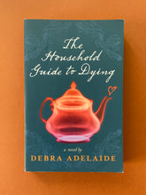 Load image into Gallery viewer, The Household Guide to Dying by Debra Adelaide: photo of the front cover which shows very minor scuff marks along the edges and a scuff mark above the letter H in the word HOUSEHOLD. There is also minor creasing on the bottom-right corner.
